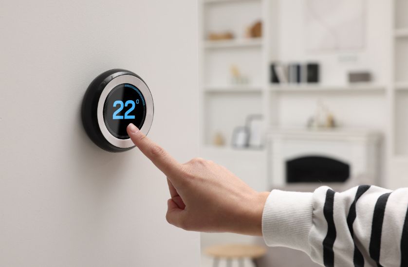 Person adjusting a smart thermostat set to 22 degrees Celsius, showcasing modern home climate control technology in a stylish living space.